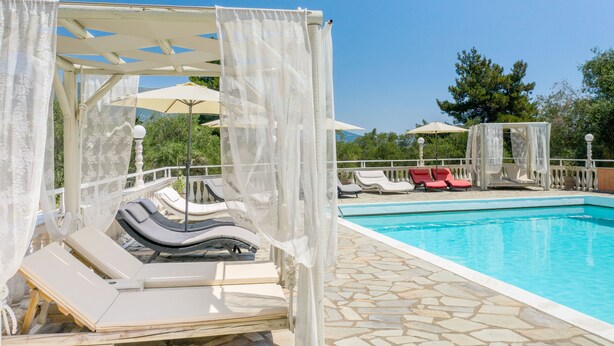 A poolside area with lounge chairs, a pool, and a pergola with white curtains. - Victoria Hill (Corfu)