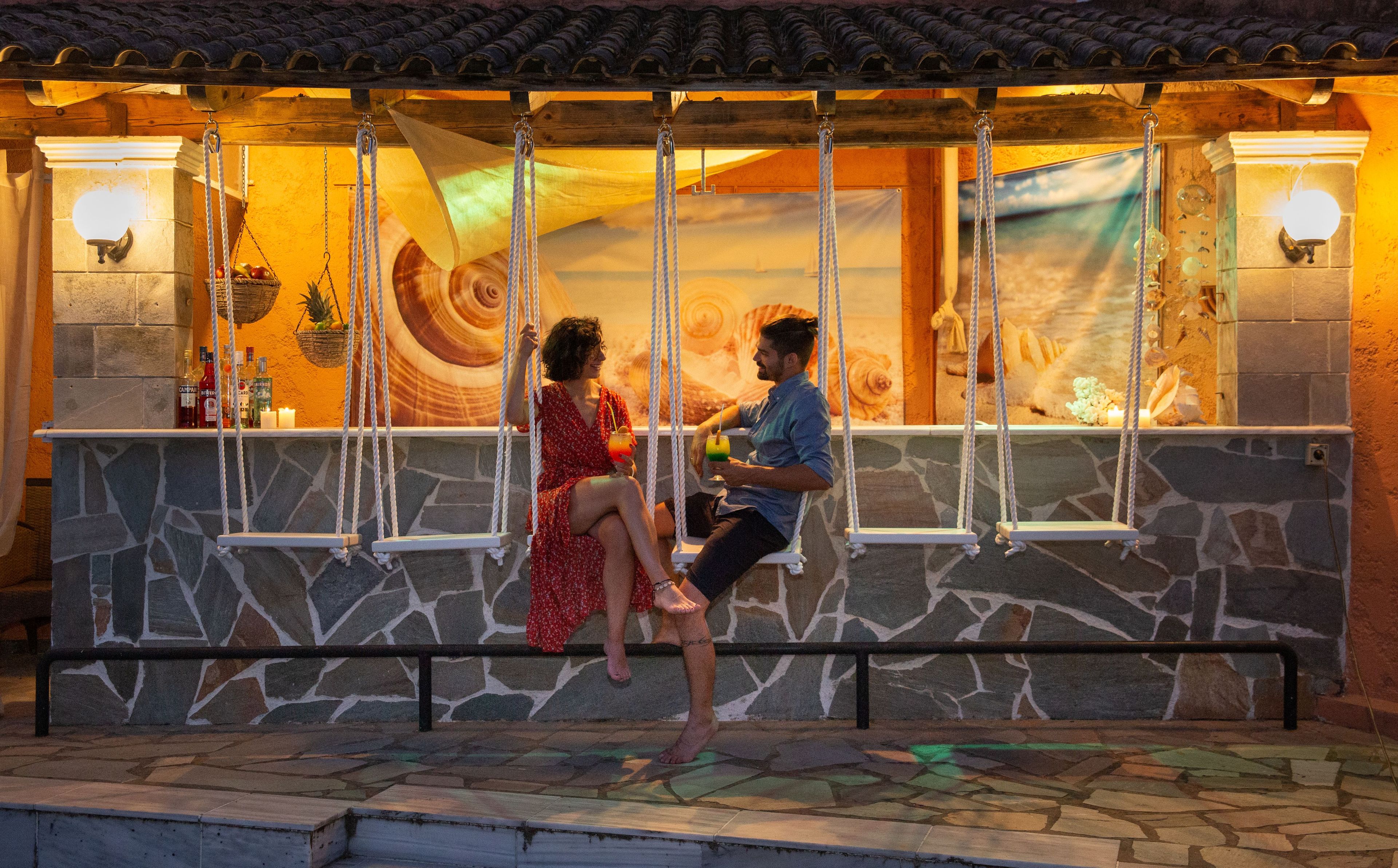 Una pareja sentada en una hamaca con un muro de piedra al fondo y un mural.