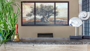 A room with a marble table, a brass bell, a green plant, a painting of a tree, and a decorative metal object. - Victoria Hill (Corfu)
