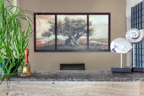 A room with a marble table, a brass bell, a green plant, a painting of a tree, and a decorative metal object.