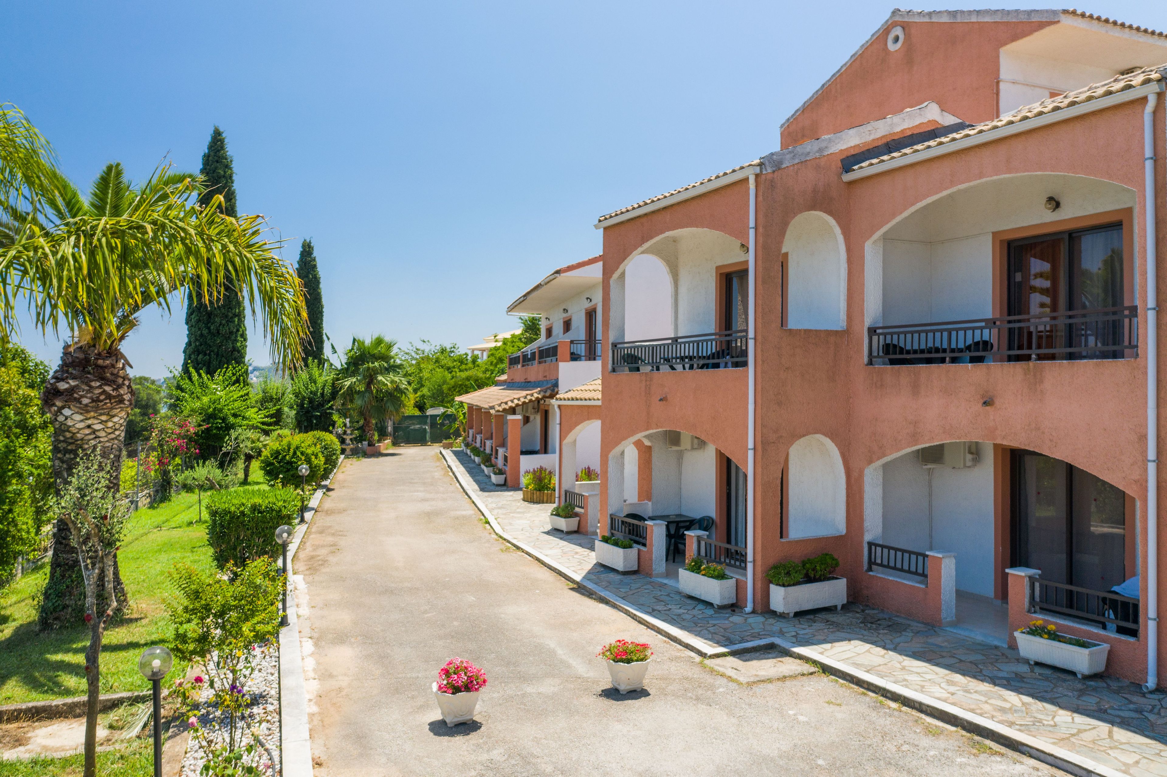 Une rangée de bâtiments de style méditerranéen, dotés de balcons et entourés de verdure et de palmiers.