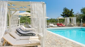 Un espace aménagé au bord de la piscine, avec des chaises longues, une piscine et une pergola agrémentée de rideaux blancs.
