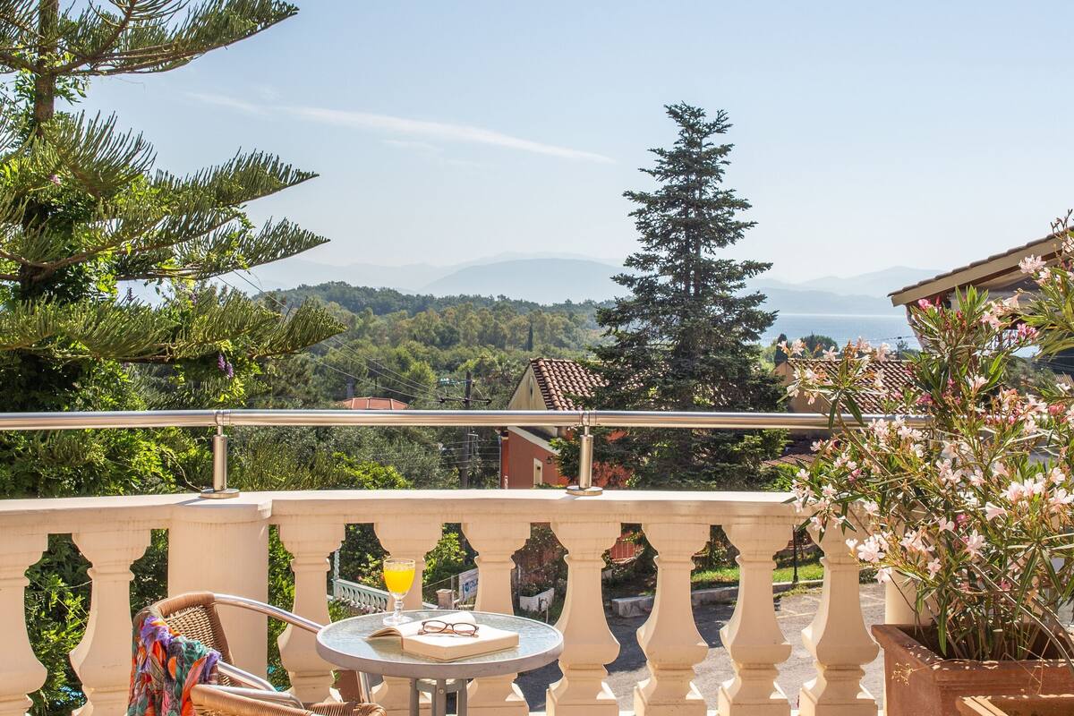 A terrace with a table and chairs, a potted plant, and a view of the landscape.