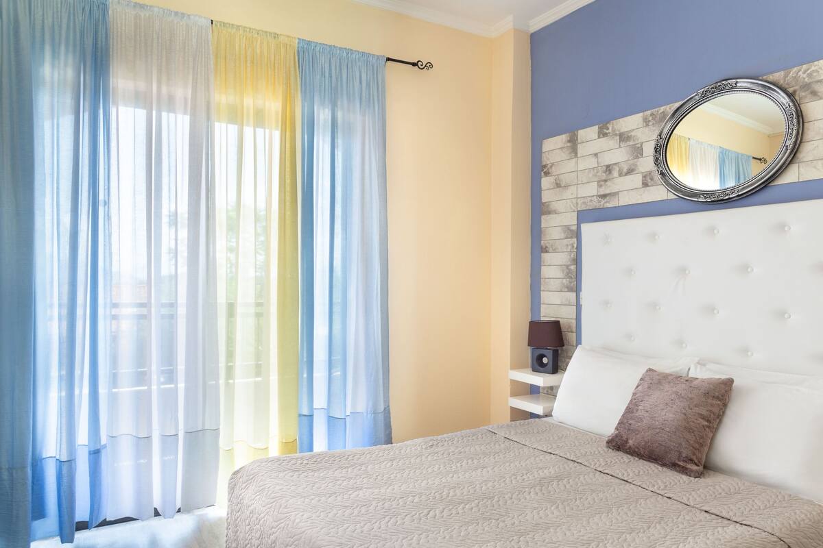 A bedroom with a large bed, a headboard, a mirror, and curtains.