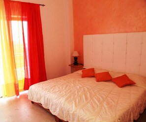 A bedroom with a bed, red curtains, a bedside lamp, and a headboard. - Victoria Hill (Corfu)