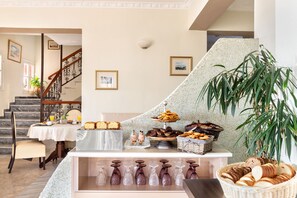 A breakfast buffet with various pastries and bread, a staircase, and a large plant.