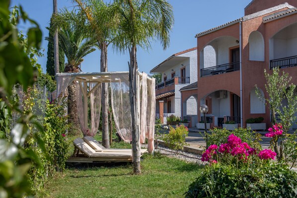 A garden with a hammock, palm trees, and a building with balconies. - Victoria Hill (Corfu)