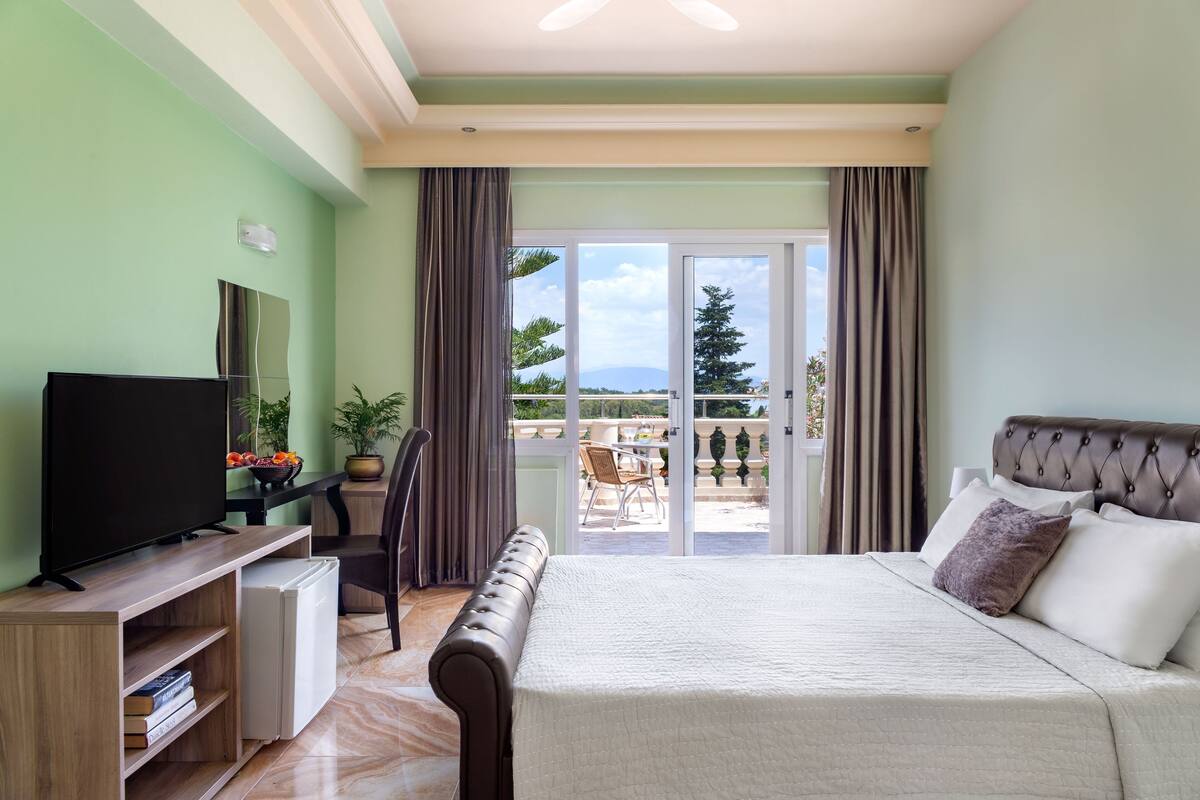A hotel room with a bed, a TV, a desk, and a balcony with a view.