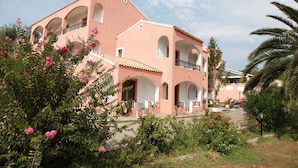 A pink building with multiple balconies and arches, surrounded by lush greenery and pink flowers. - Victoria Hill (Corfu)