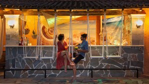 Un couple est assis sur une balançoire, avec un mur de pierre et une fresque en arrière-plan.