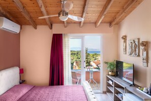 A bedroom with a bed, a ceiling fan, a TV, a sliding glass door to a balcony, and a view of the landscape. - Victoria Hill (Corfu)