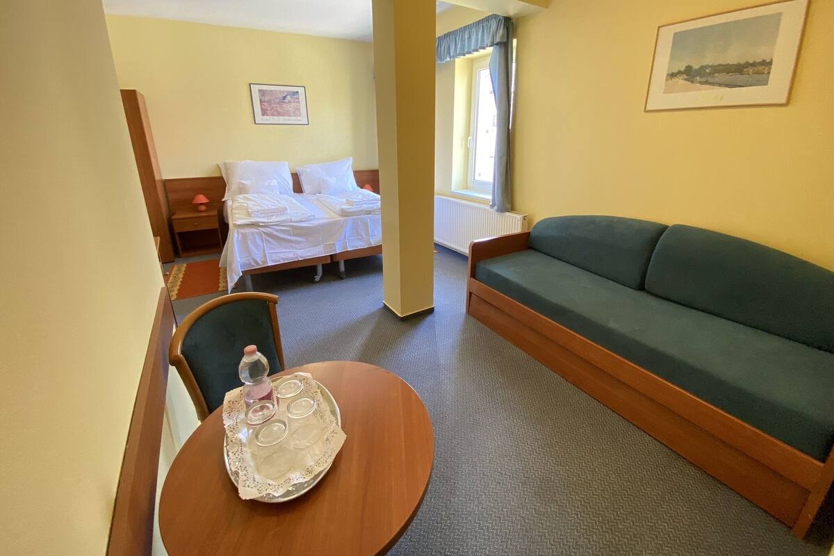 A hotel room with a bed, a green sofa, a round wooden table with a tray, and a chair.