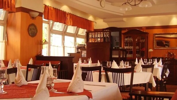 Een restaurant met meerdere gedekte tafels, met witte tafelkleden en servetten.