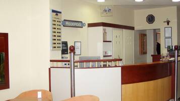 Zona de recepción con un mostrador de madera, un reloj y un letrero que dice “RECEPCIÓN”.