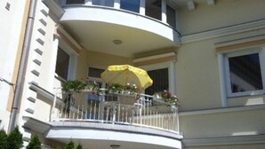 Een gebouw met twee verdiepingen, met een balkon op de tweede etage, voorzien van een gele parasol en plantenpotten.