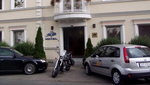 A hotel with a balcony, a motorcycle, and a car parked in front.