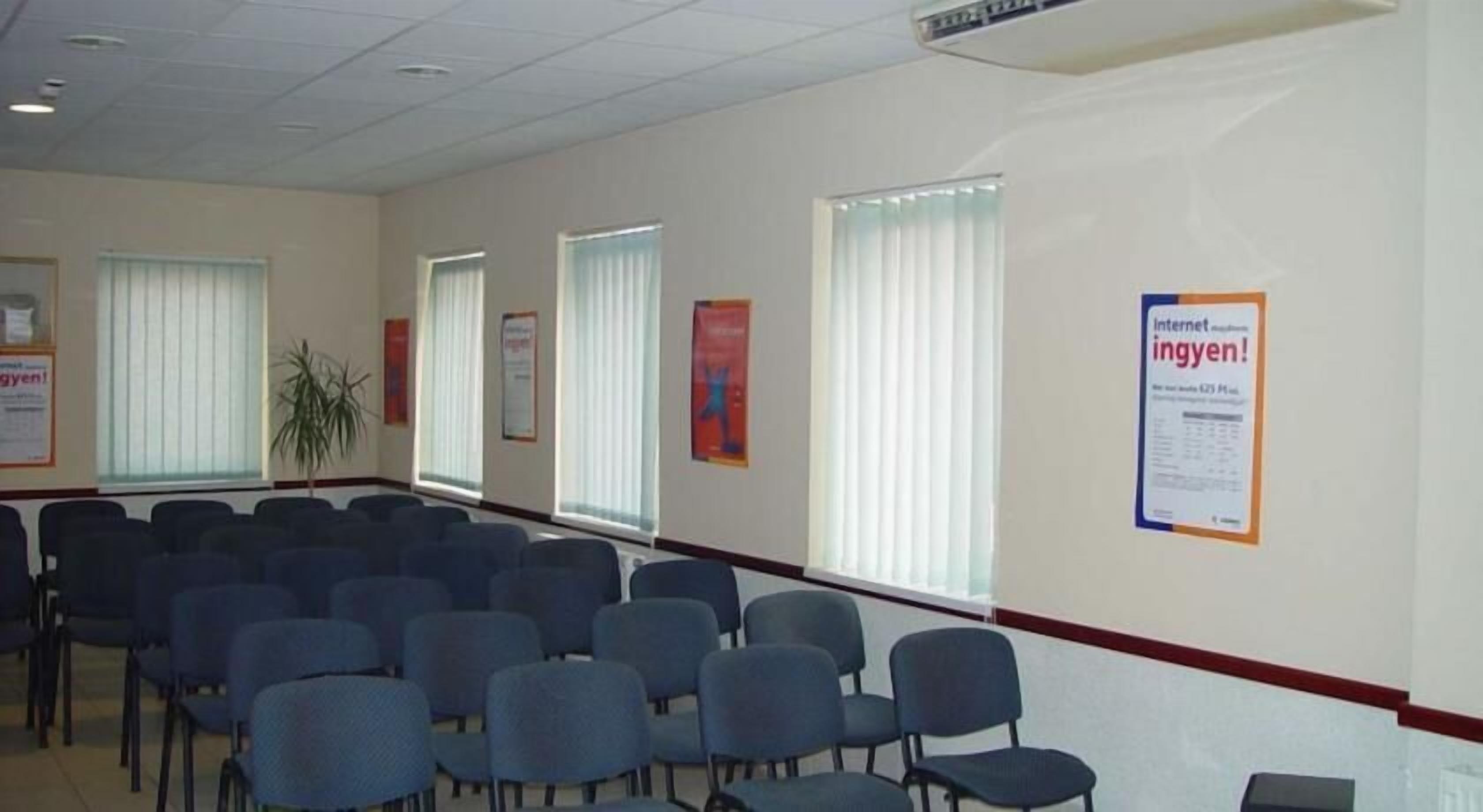 A conference room with rows of chairs, large windows with blinds, and informational posters on the walls.
