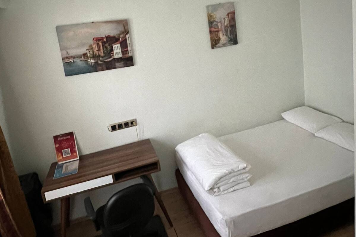 Ein Hotelzimmer mit einem Einzelbett, einem Schreibtisch mit Stuhl und zwei an der Wand hängenden Bildern.