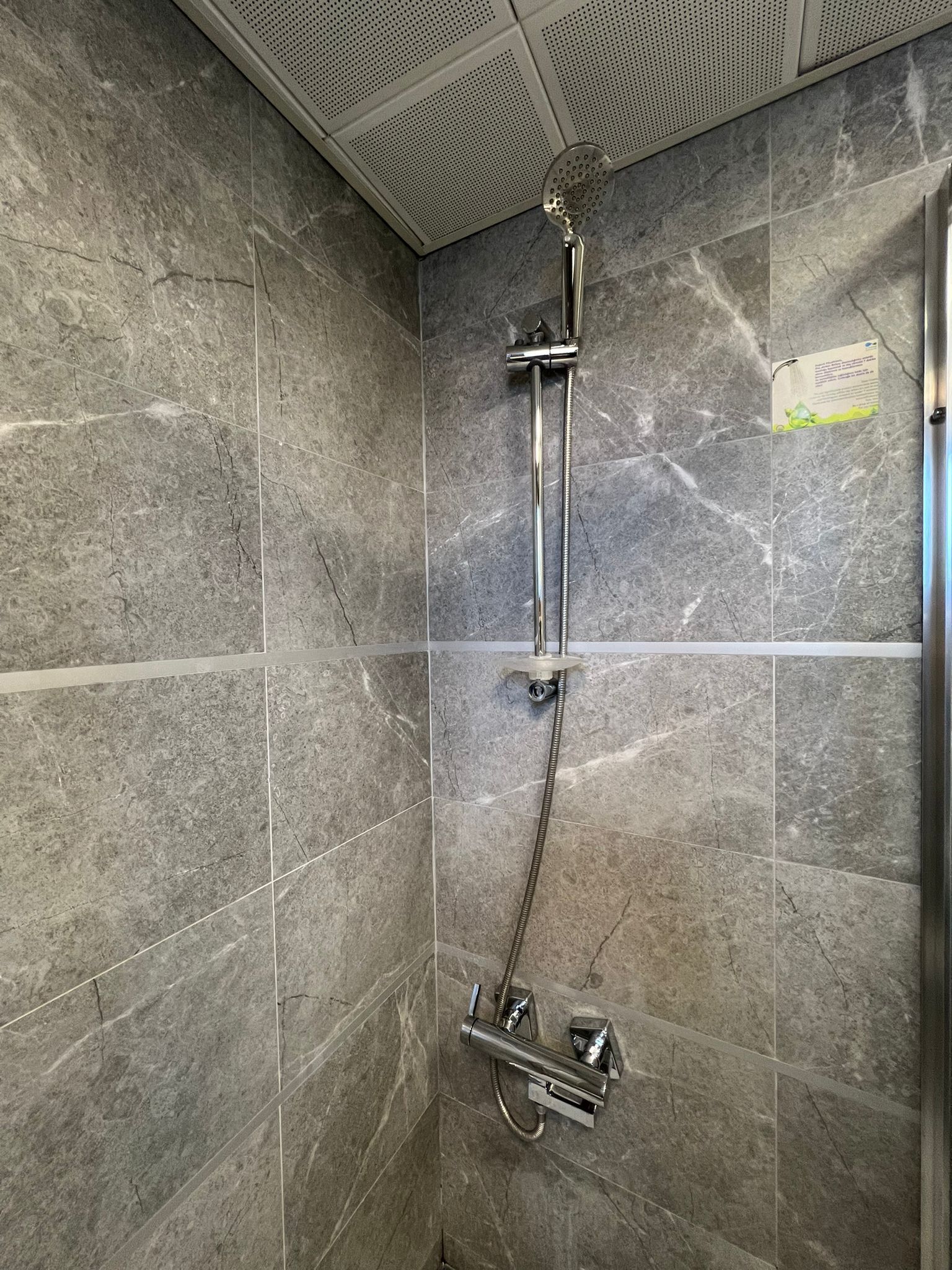 Eine Dusche mit Handbrause und fest installierter Duschköpfe, beide an einer Wand unter einer Lochplatte.
