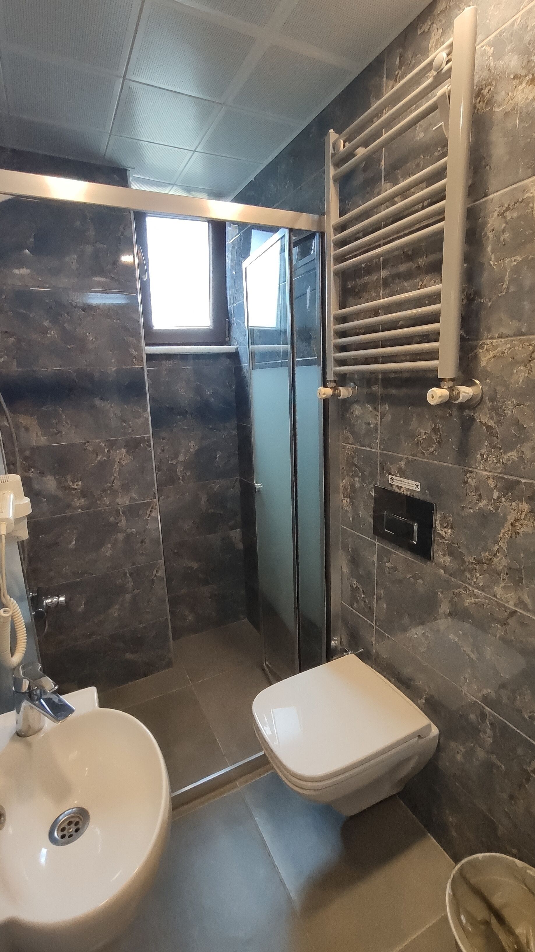 A bathroom with a shower, toilet, sink, and a towel rack.