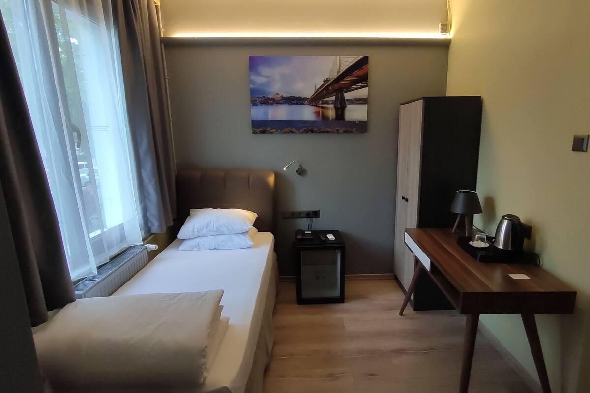 Ein Hotelzimmer mit Bett, Nachttisch, Lampe und einem Bild einer Brücke.