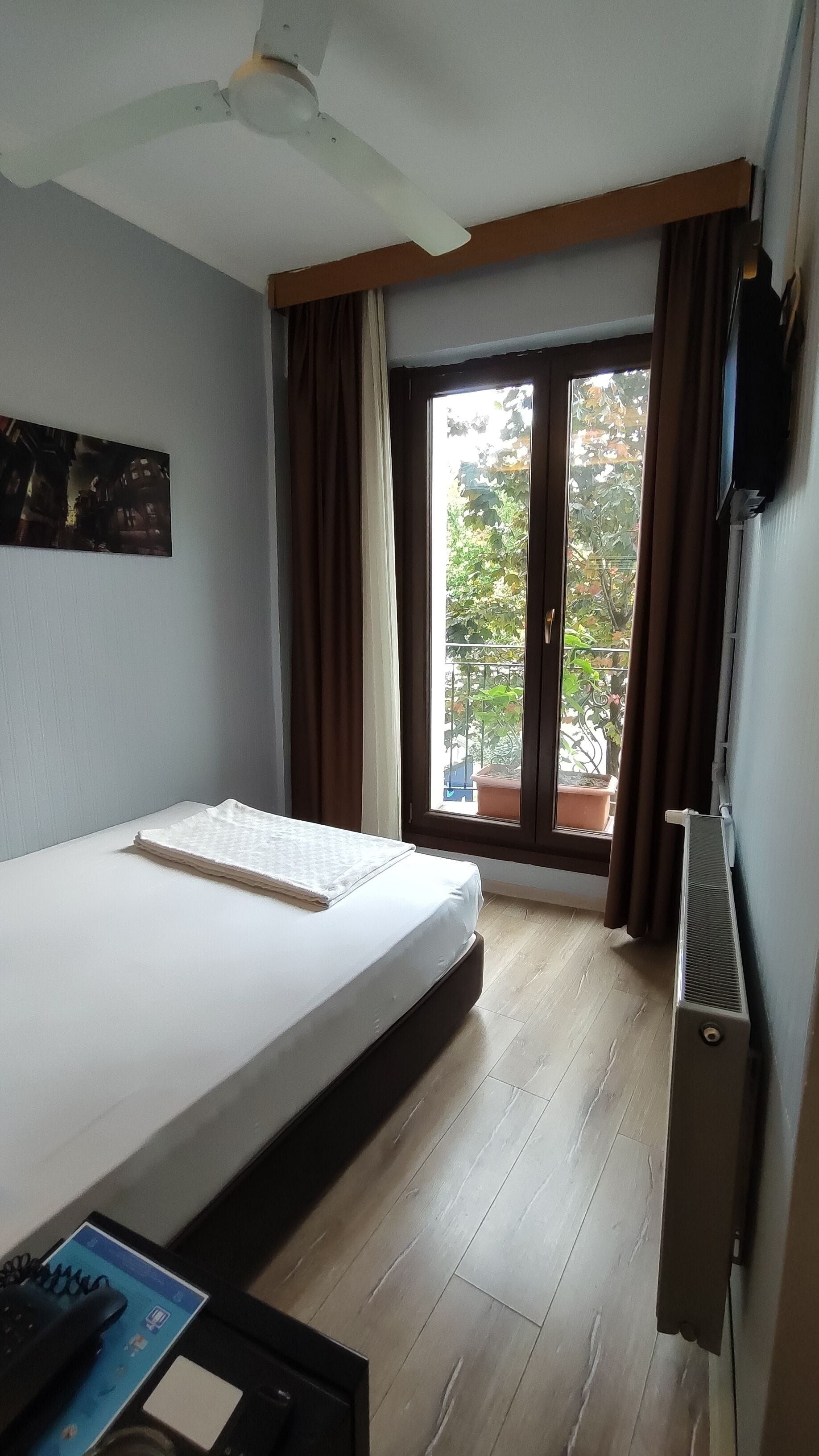 Een hotelkamer met een bed, een bureau met telefoon, een radiator en uitzicht op het buiten.
