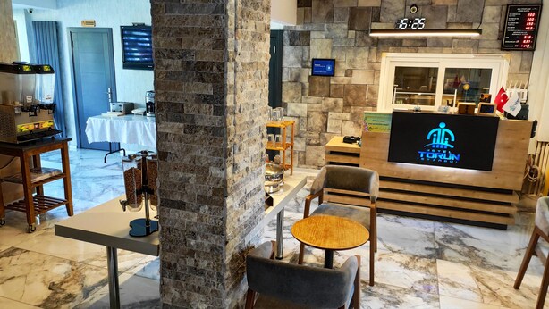 A hotel reception area with a stone wall, a digital screen displaying the hotel name, a coffee machine, and a seating area with tables and chairs. - Hotel Torun Istanbul Old City (Istanbul)
