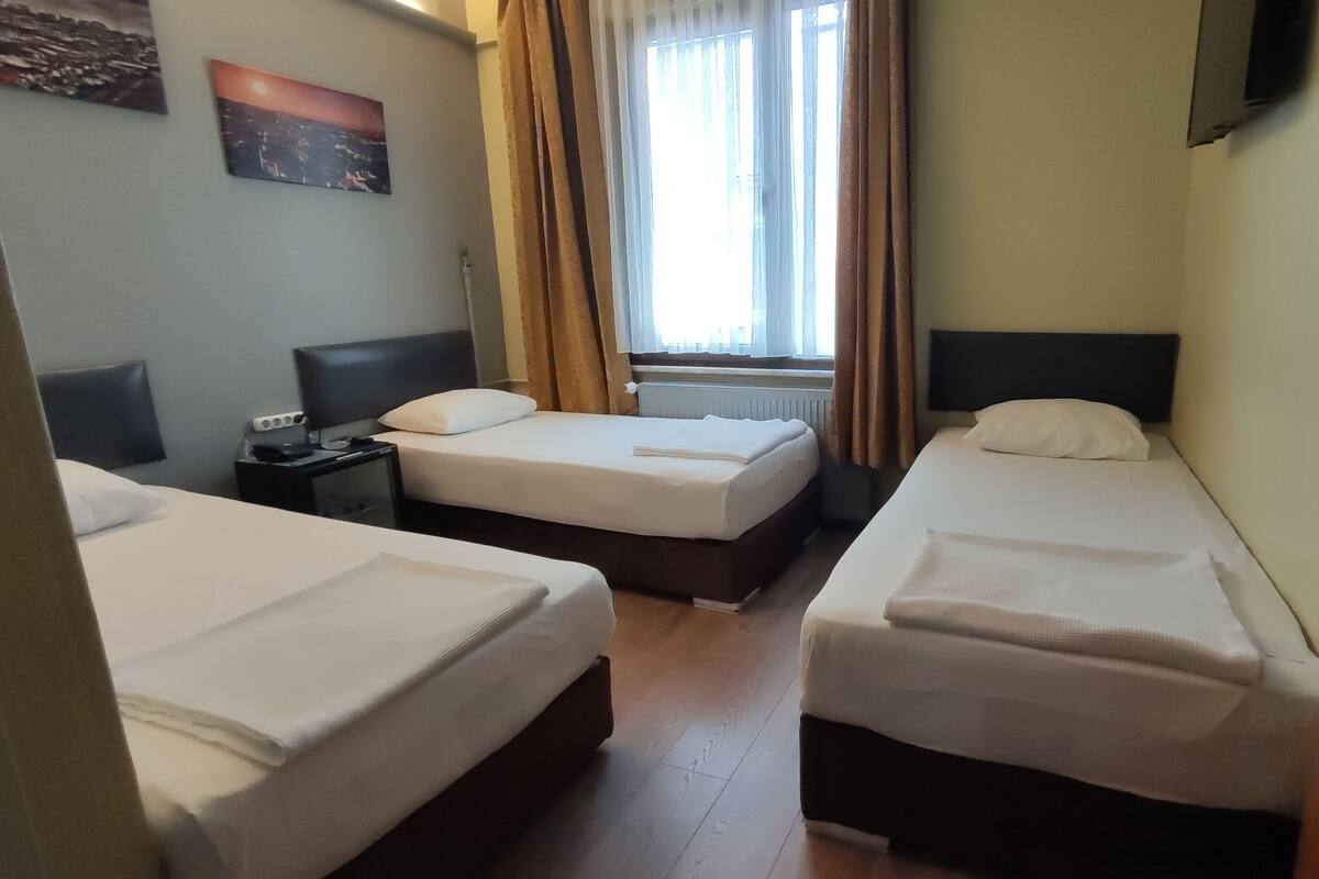 Ein Hotelzimmer mit zwei Einzelbetten, einem Nachttisch mit Lampe, einem Fenster mit Vorhängen und einem Bild an der Wand.
