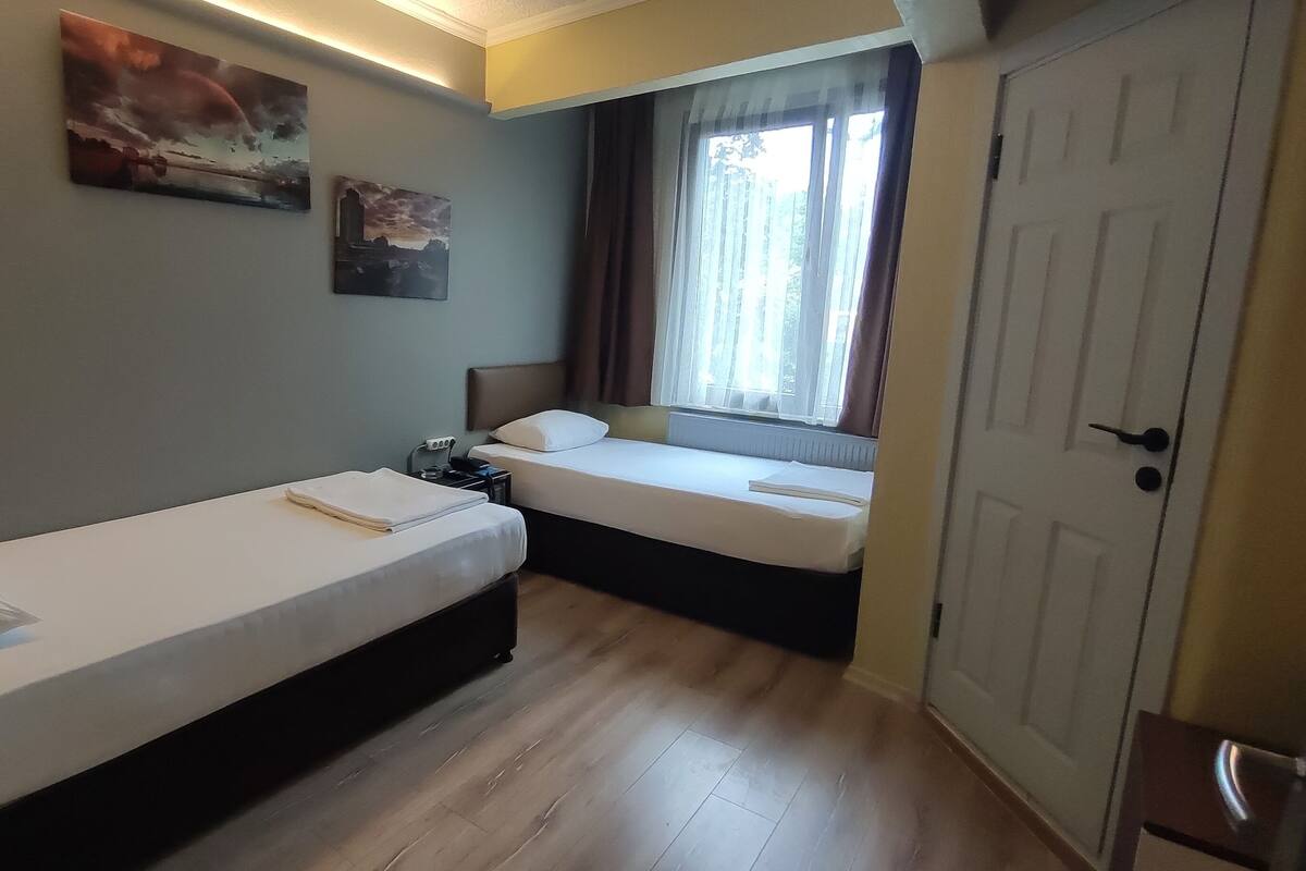 Ein Schlafzimmer mit zwei Einzelbetten, einem Nachttisch mit Lampe, einem Fenster mit Vorhängen und einer Tür.