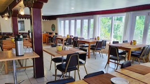 Un área de comedor con varias mesas y sillas, una máquina de café y vistas a zonas verdes.