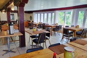 A dining area with multiple tables and chairs, a coffee machine, and a view of greenery outside.