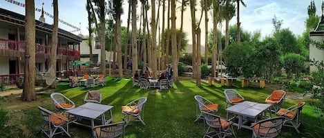 A courtyard with outdoor seating, a building with a balcony, and tall trees.