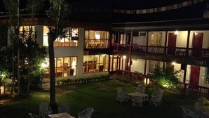 Un bâtiment à deux étages, doté de nombreuses fenêtres et de balcons, entouré d’un espace extérieur bien éclairé, aménagé avec des chaises et des tables.
