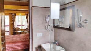 Une chambre d’hôtel avec un lit, une salle de bain avec un lavabo et un miroir, et une fenêtre avec des rideaux.