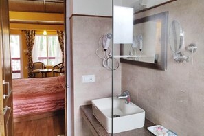 A hotel room with a bed, a bathroom with a sink and mirror, and a window with curtains. - Hotel Shambhala Resort (Leh)