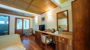 Une chambre à coucher avec un lit, un bureau avec une télévision, une chaise, un miroir et une fenêtre.
