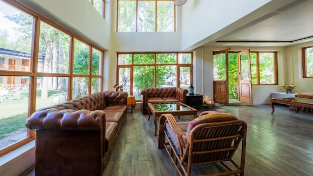 Una habitación amplia con ventanas grandes, un sofá de cuero, una mesa de madera y sillas de mimbre.