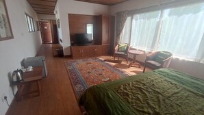 Una habitación con cama, televisión, una mesita, una silla y ventana.