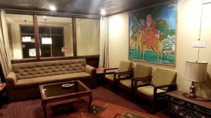 A living room with a sofa, chairs, a coffee table, a lamp, and a wall painting. - Hotel Shambhala Resort (Leh)