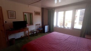 A room with a bed, a desk with a television, a chair, and a window with curtains. - Hotel Shambhala Resort (Leh)