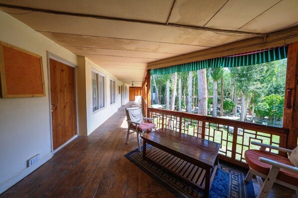 A covered porch with wooden flooring, a bench, chairs, and a view of trees. - Hotel Shambhala Resort (Leh)