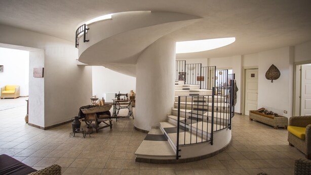 A spacious living area with a curved staircase, a dining table, and a yellow armchair. - Hotel Su Baione (Abbasanta)