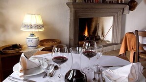 A dining table set with wine glasses, plates, and cutlery, a lamp, and a fireplace in the background. - Hotel Su Baione (Abbasanta)