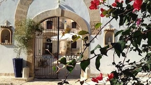 Une entrée en arc donnant sur un bâtiment, avec une allée bordée de portails, des plantes en pot et une vue dégagée sur l’intérieur à travers l’arc.