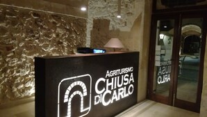 Un comptoir d’accueil avec un mur en pierre en arrière-plan et une enseigne indiquant « Agriturismo Chusá DICARLO ».