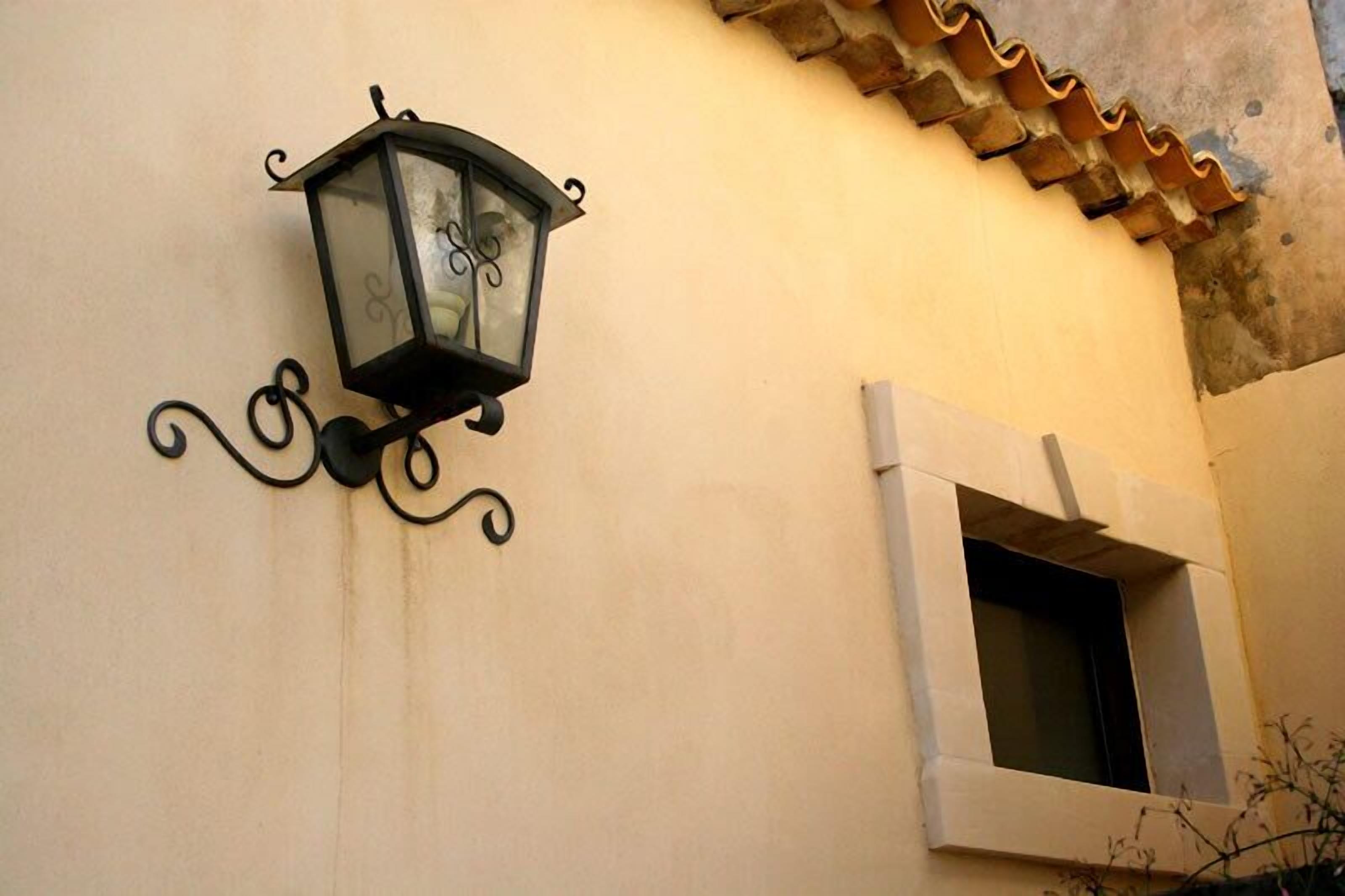 A wall-mounted lantern with a decorative design, a window with a white frame, and a tiled roof.
