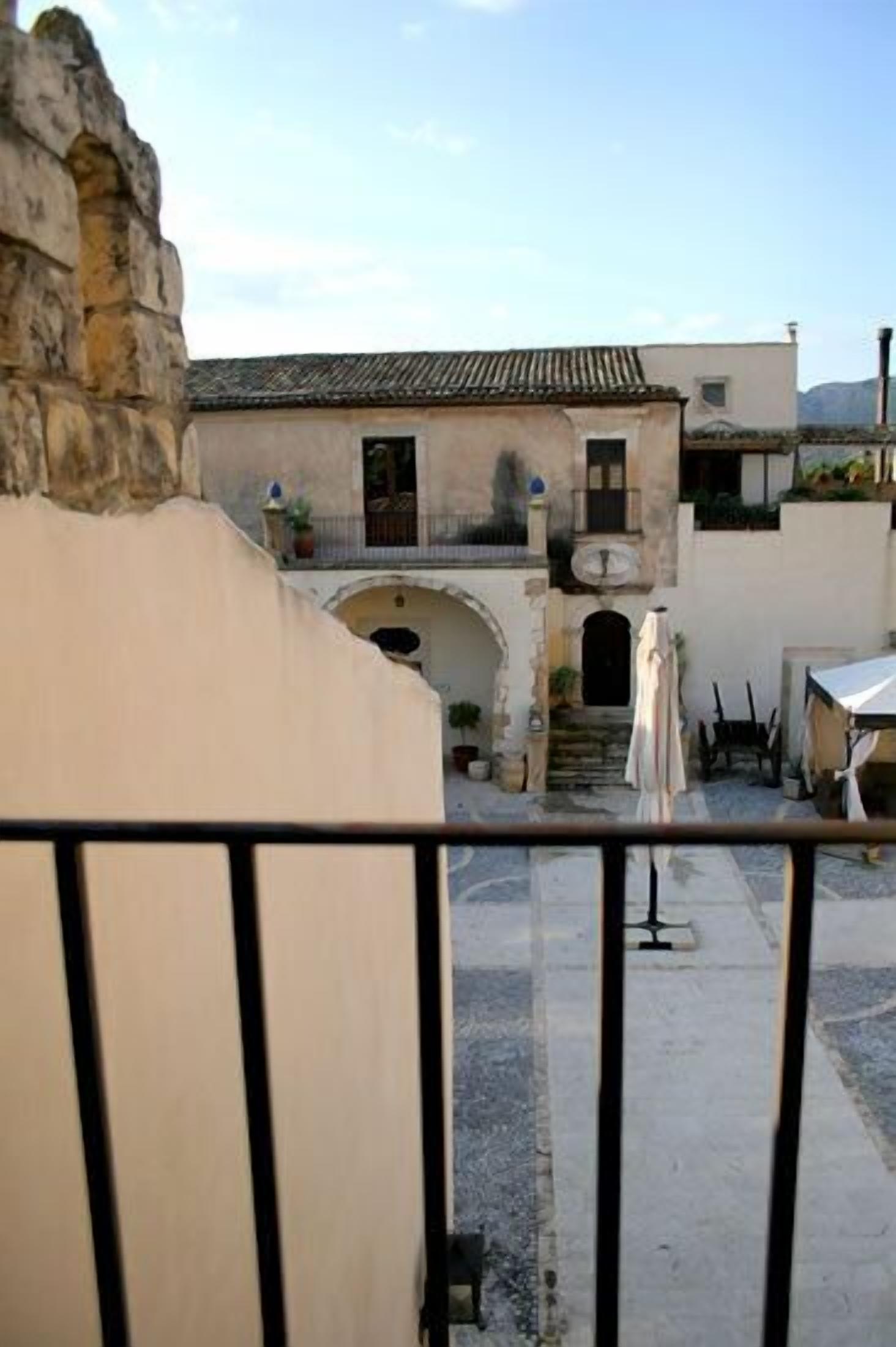 A courtyard with a building featuring a tiled roof, stone walls, and a small balcony.