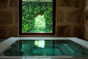 A spa area with a hot tub and a view of a lush green tree through a window. - Agriturismo Chiusa di Carlo (Avola)