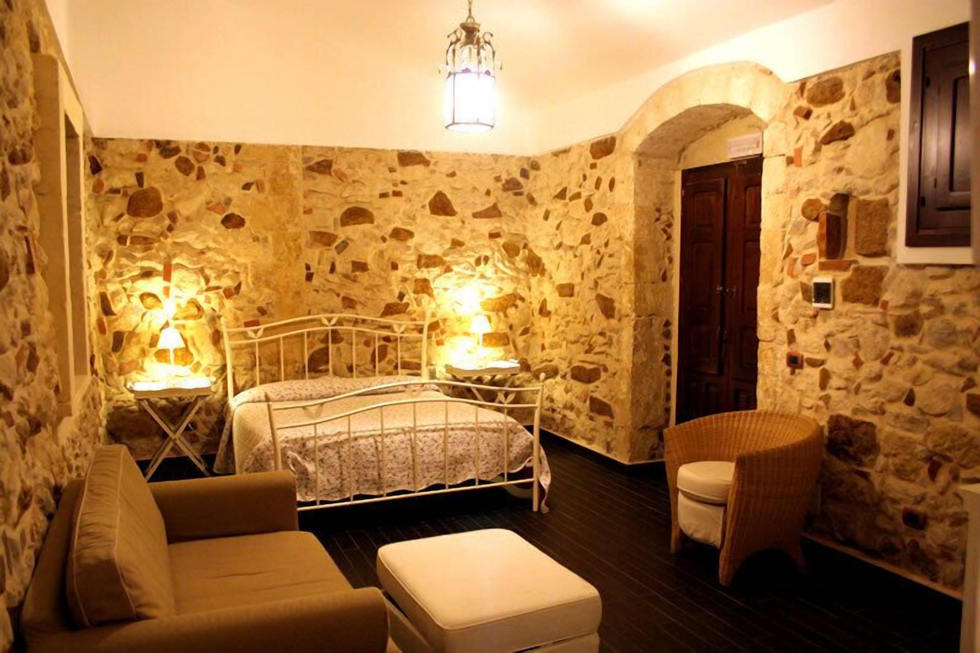 Camera con pareti in pietra, un letto, due lampade da comodino, una sedia e un tavolino.