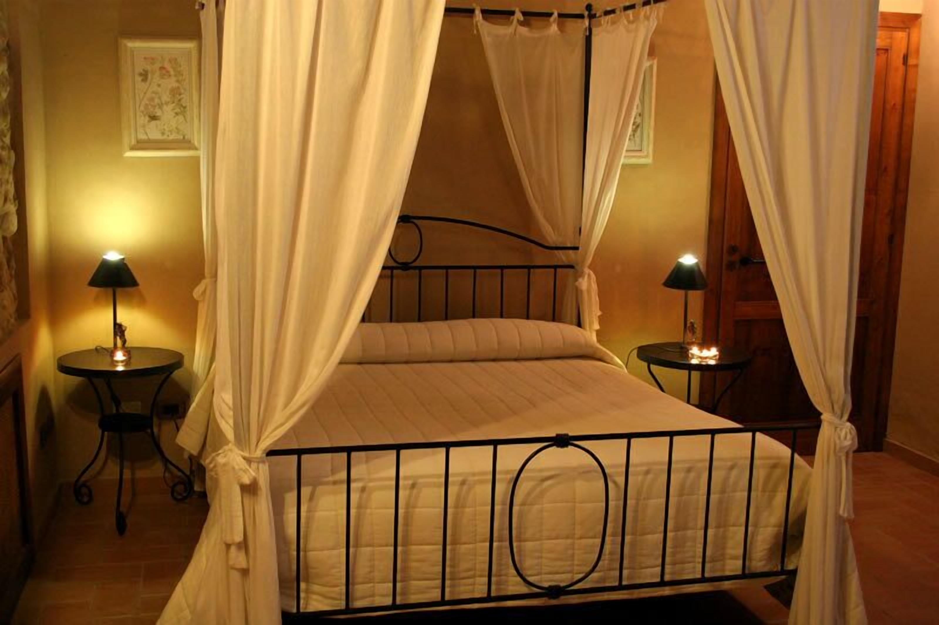 A four-poster bed with white curtains, two bedside tables with lamps, and a framed picture on the wall.
